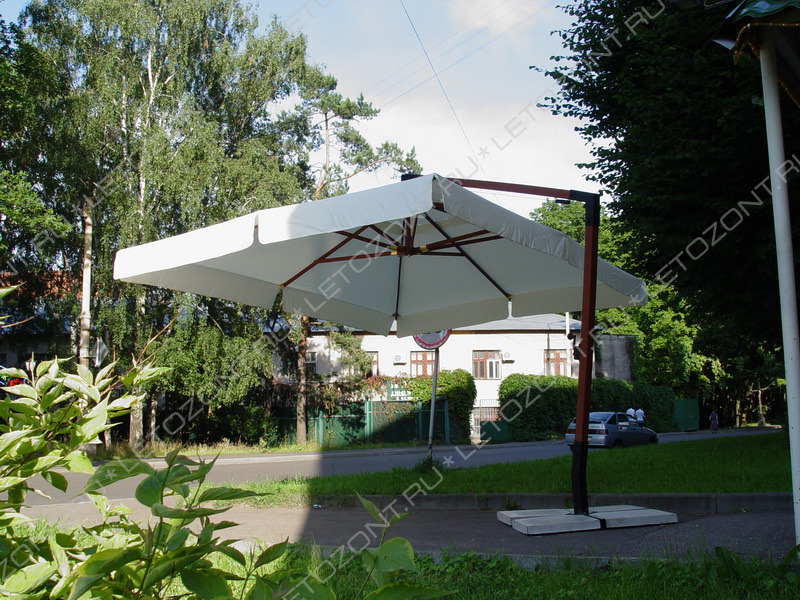 Фото большого зонта с боковой опорой на улице. Цвет светлобежевый
